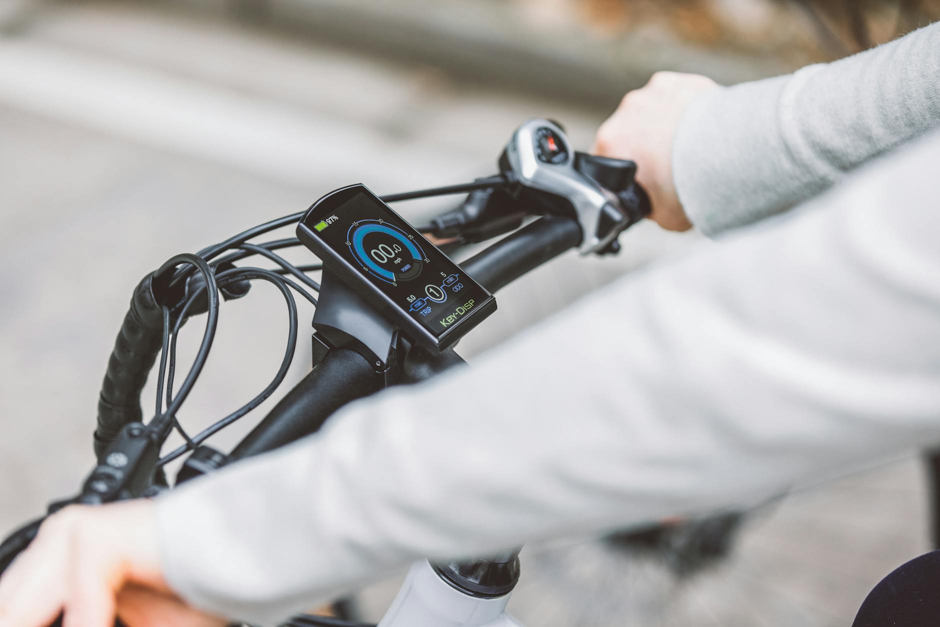Hands gripping the handlebar of an electric bicycle, showcasing the digital display screen for speed and battery status.